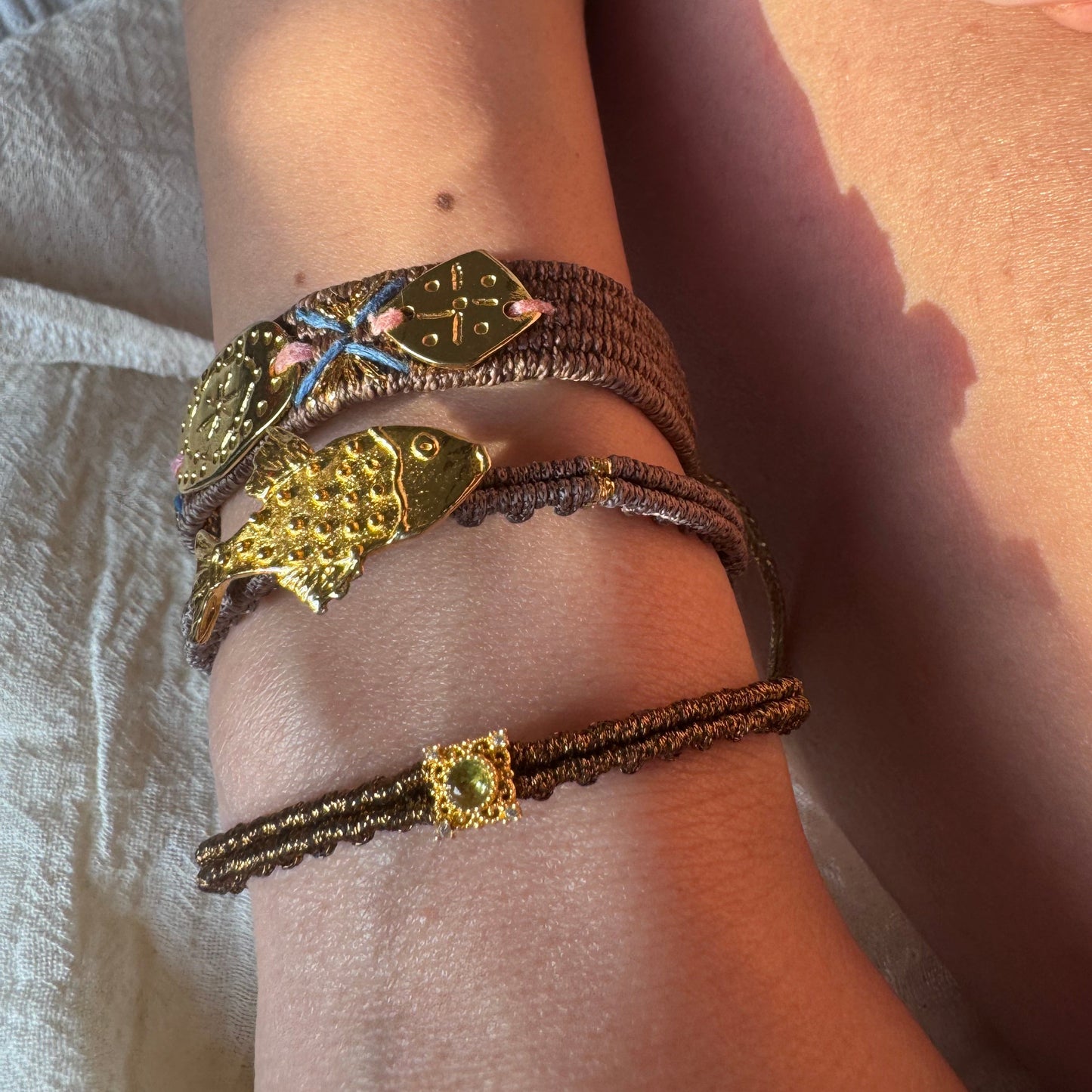 Close-up of a wrist wearing two gold bracelets with intricate designs on a neutral background.