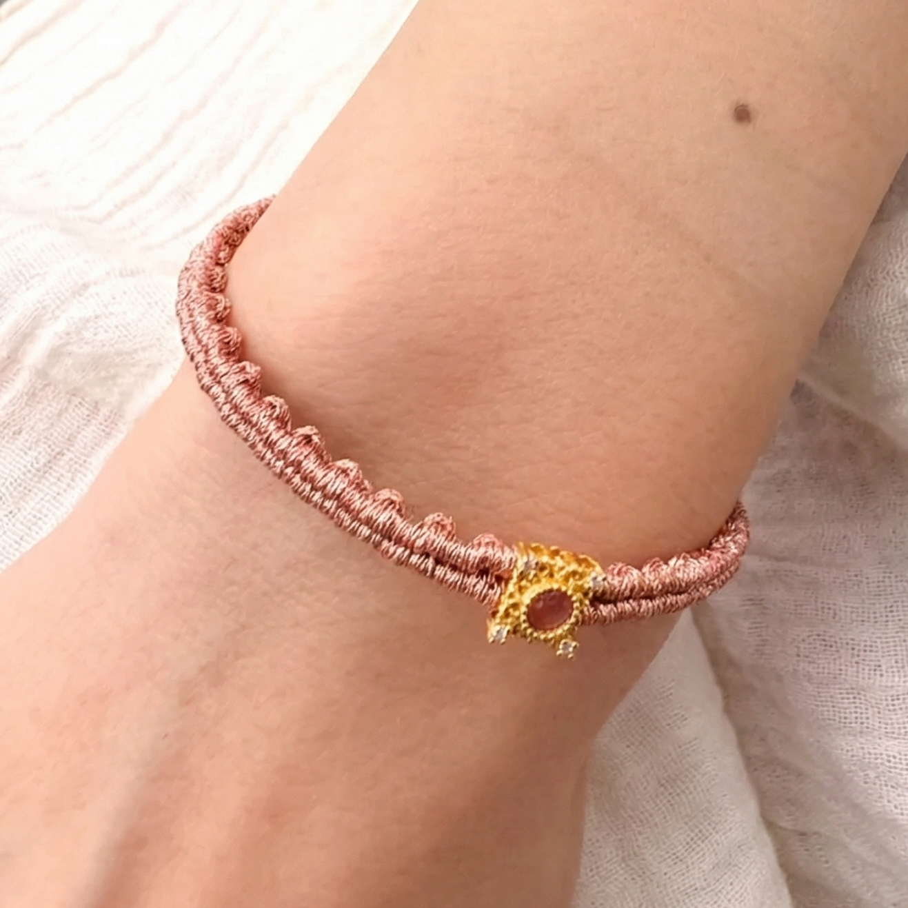 a pink beaded handwoven bracelet with a sun charm.