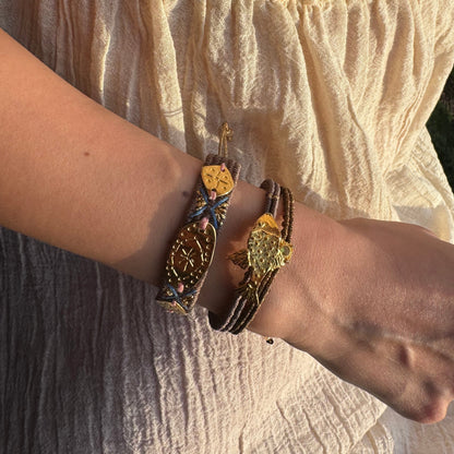 Close-up of a wrist wearing multiple bracelets with intricate designs on a textured fabric background.