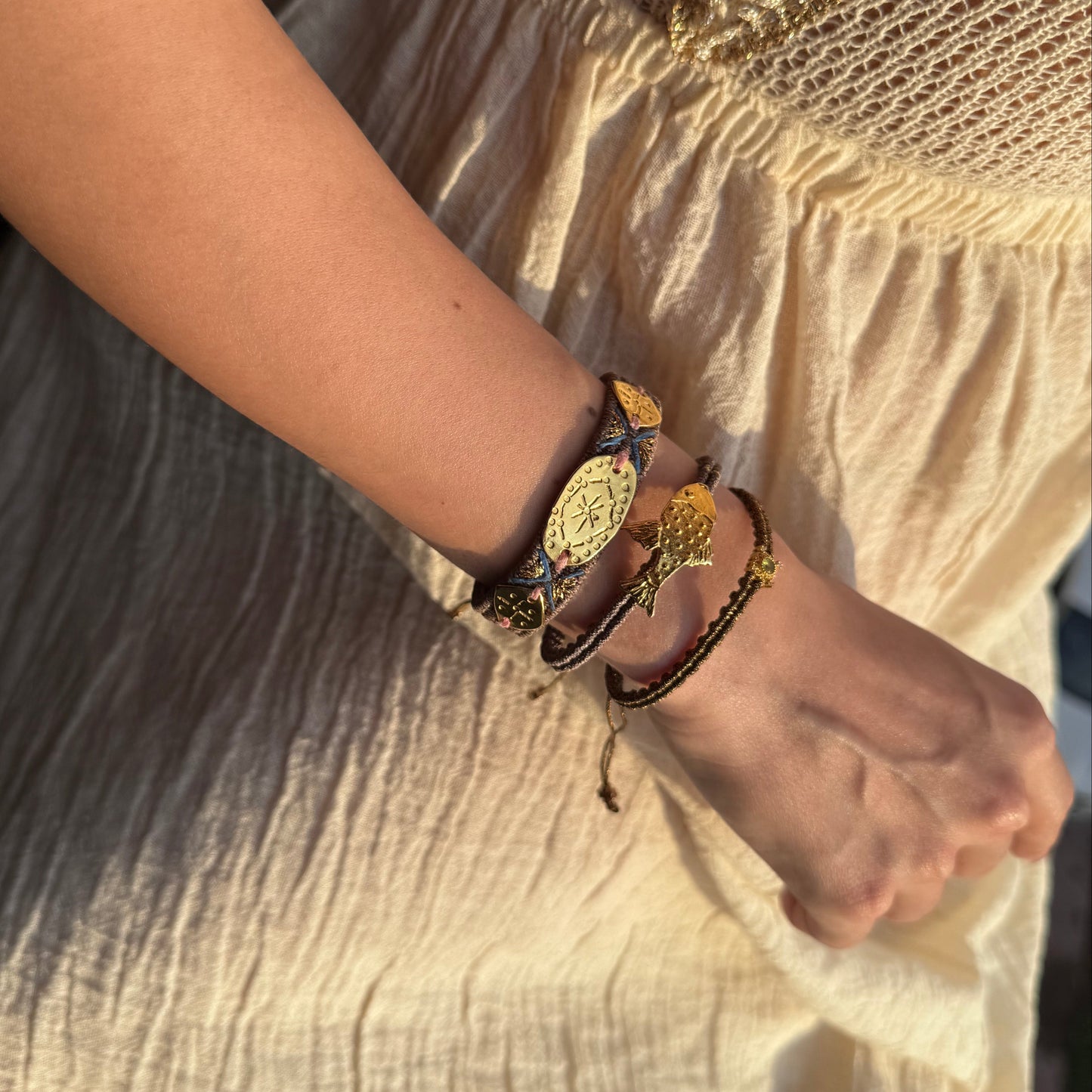 Close-up of a person's arm wearing multiple bracelets on a light fabric background