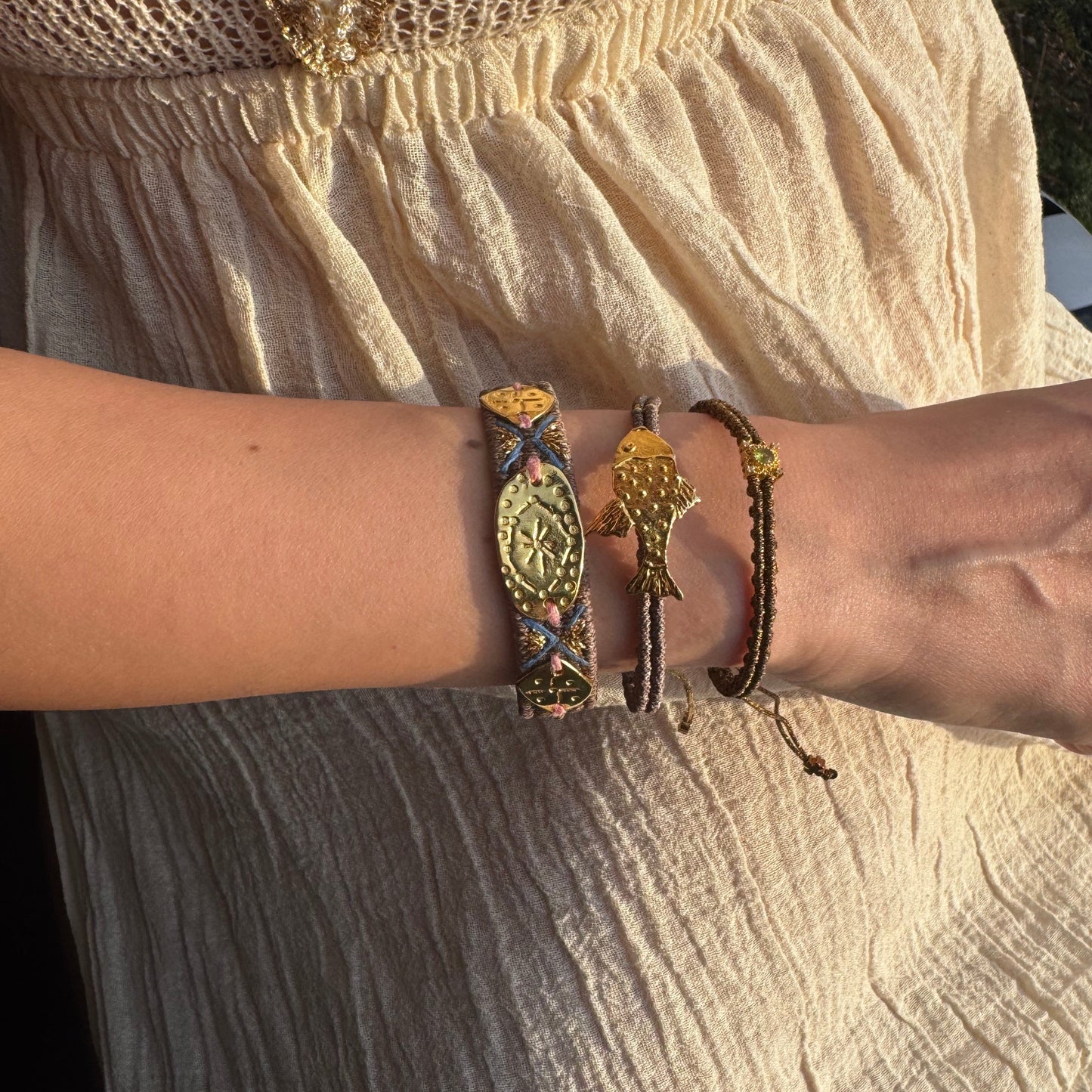 Close-up of a wrist wearing multiple bracelets with intricate designs on a textured fabric background.