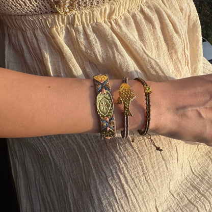Close-up of a wrist wearing multiple bracelets with intricate designs on a textured fabric background.
