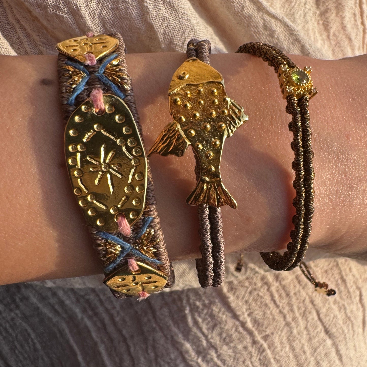 Bracelet with gold fish charm on a wrist against a textured fabric background