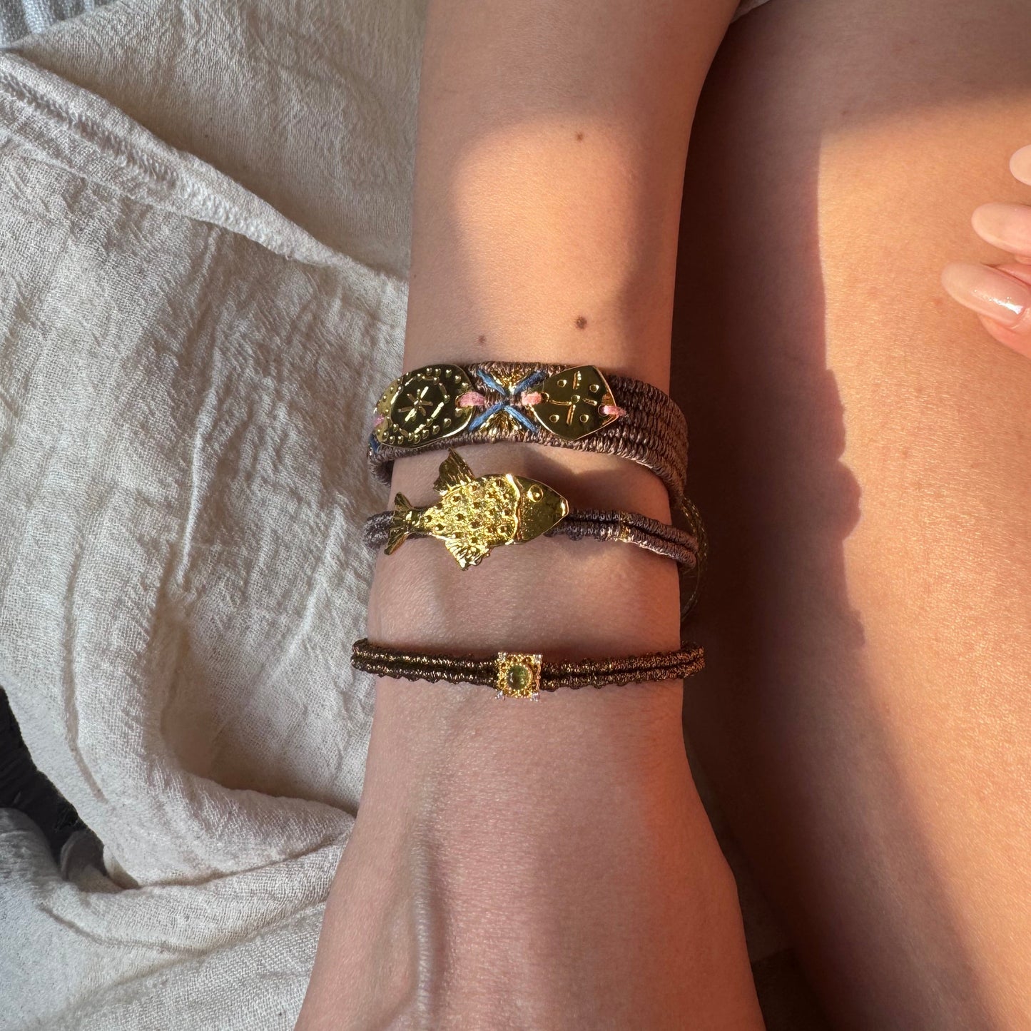 Close-up of a person's wrist wearing multiple bracelets on a light fabric background