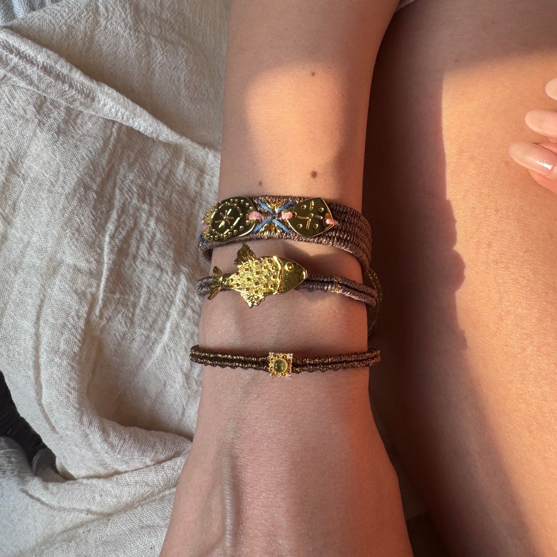 Close-up of a person's wrist wearing multiple bracelets on a light fabric background
