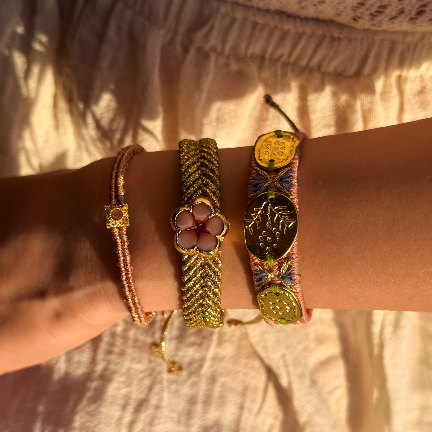 Close-up of a wrist wearing multiple gold bracelets with intricate designs on a neutral background.