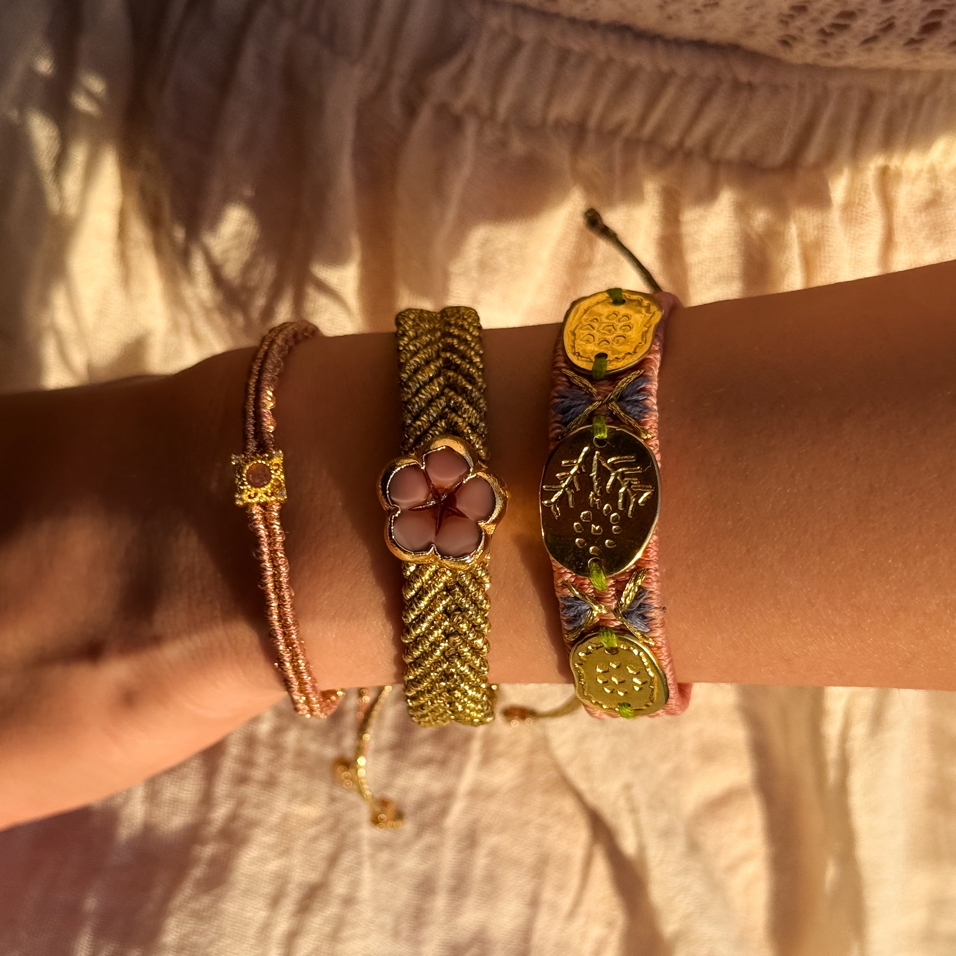 Close-up of a wrist wearing multiple gold bracelets with intricate designs on a neutral background.
