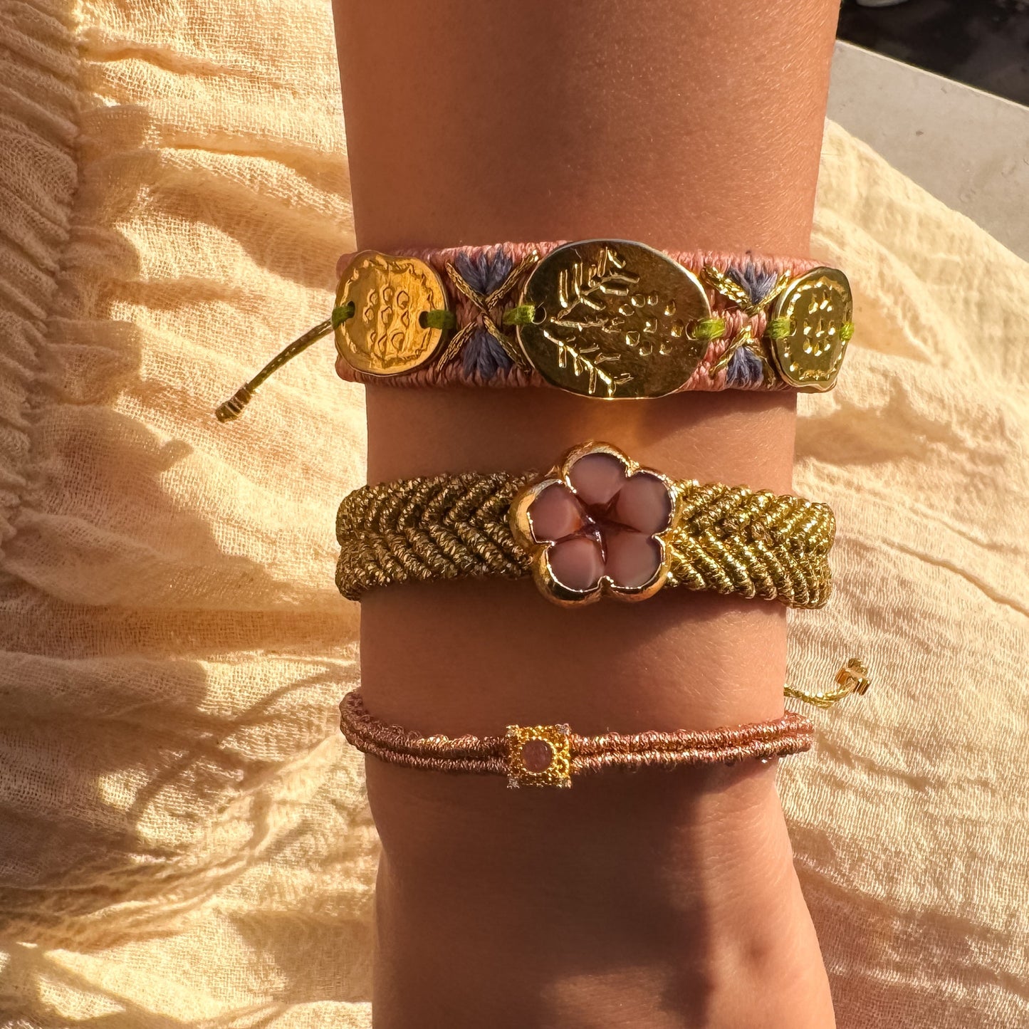 Close-up of a wrist wearing three decorative bracelets on a textured fabric background