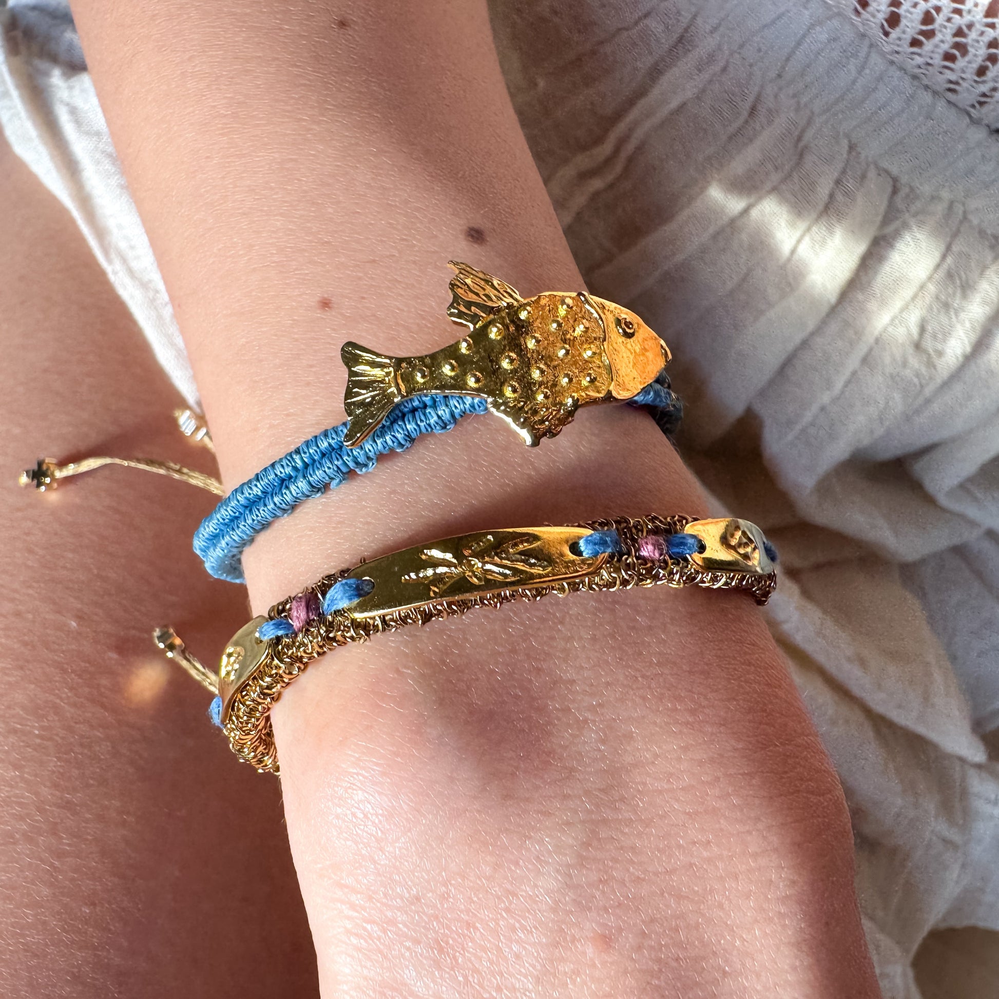 Close-up of a wrist wearing gold and blue bracelets with decorative elements.