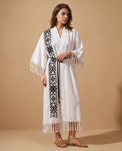 Woman wearing a white kimono with black geometric patterns and fringes on a beige background
