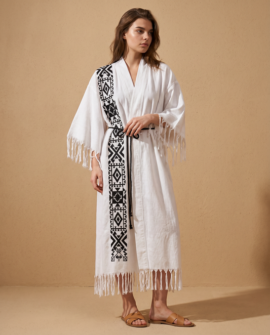 Woman wearing a white kimono with black geometric patterns and fringes on a beige background